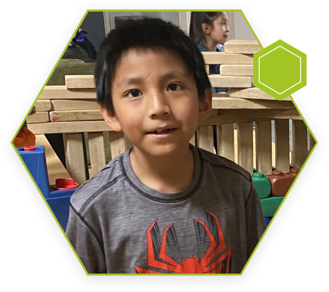 A young boy is standing in front of some wooden blocks.