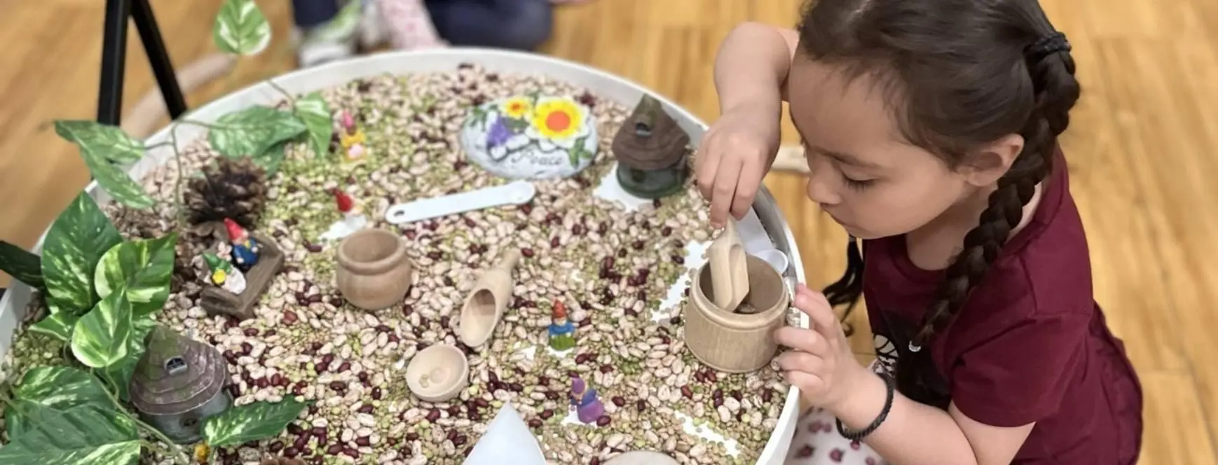 A child playing with a tray of rice and other items.