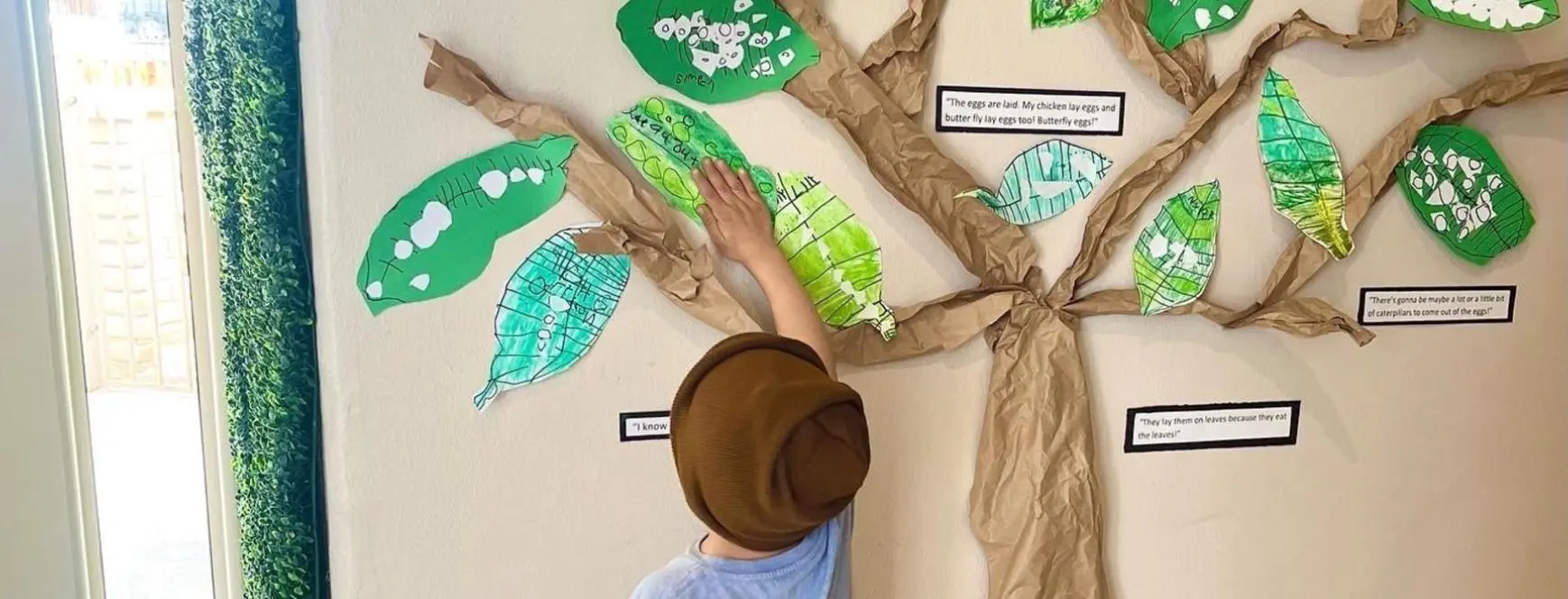 A child reaching for leaves on the wall