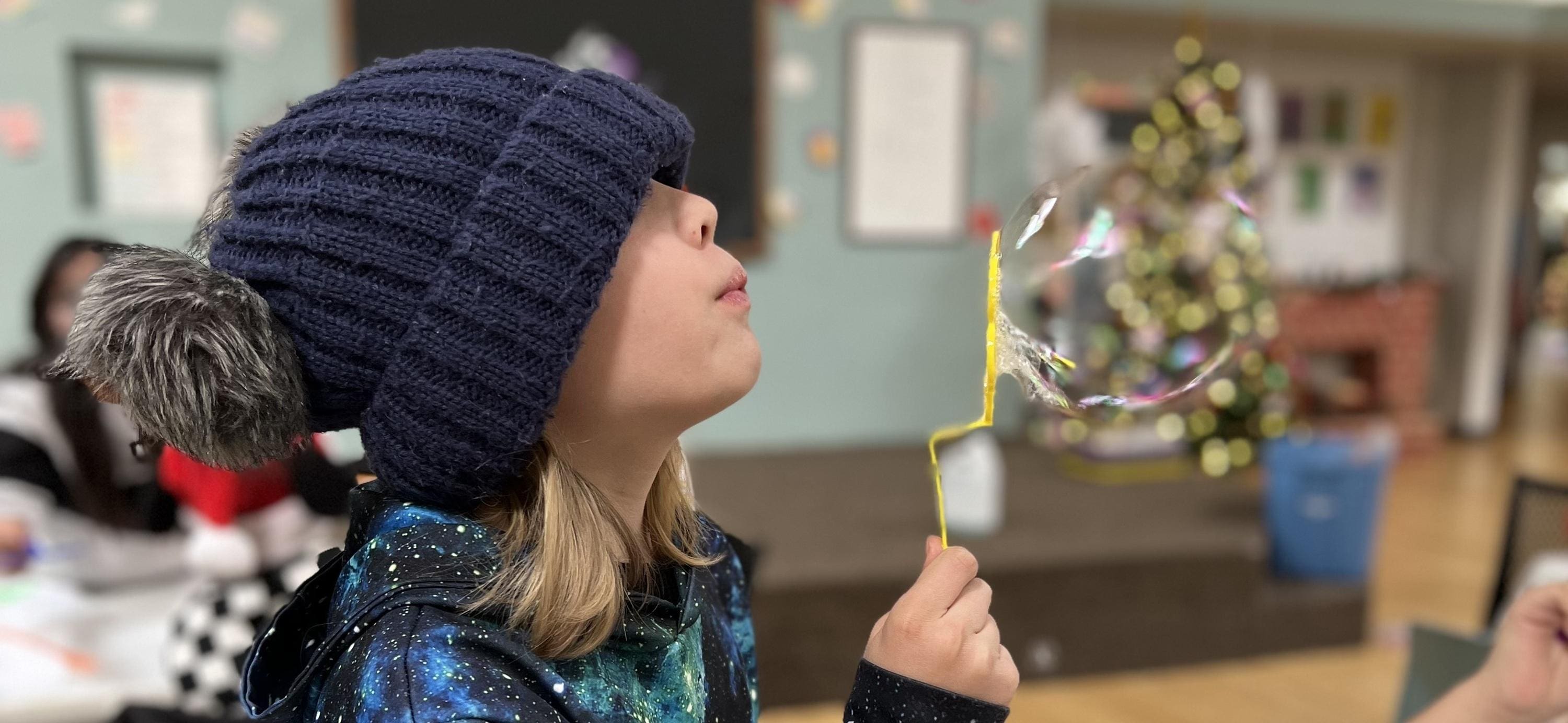 A child blowing bubbles with a yellow wand.